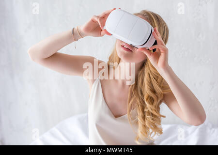 Elegante Frau mit Virtual reality Headset auf dem Bett Stockfoto