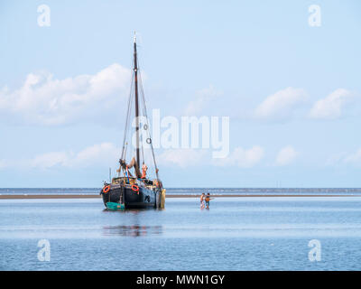 Junge Männer das Waten im seichten Wasser in der Nähe von Sand flach und Segelyacht Schiffbruch bei Ebbe am Wattenmeer, Niederlande Stockfoto