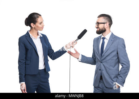 Lächelnd weibliche Journalisten interviewen Geschäftsmann in Anzug, isoliert auf weißem Stockfoto