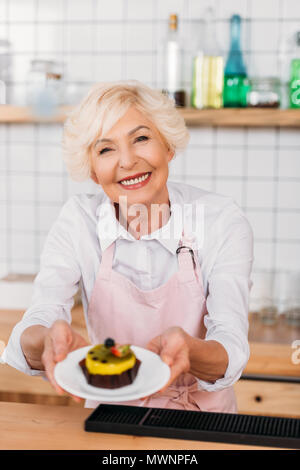 Portrait von lächelnden Coffee Shop Arbeiter in Schürze Halteplatte mit Dessert in den Händen Stockfoto