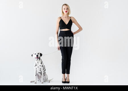 Attraktive stilvolle blonde Frau in schwarzer Kleidung mit Dalmatiner Hund auf Weiß Stockfoto