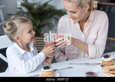 Glückliche Mutter und Tochter Anstoßen mit Saft beim Frühstück zu Hause Stockfoto