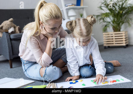 Junge Mutter mit niedlichen kleinen Tochter lernen Zahlen beim Sitzen auf dem Boden zu Hause Stockfoto