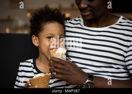 7/8 Schuß von Happy african american Vater Fütterung niedlichen kleinen Sohn mit Eis im Cafe Stockfoto