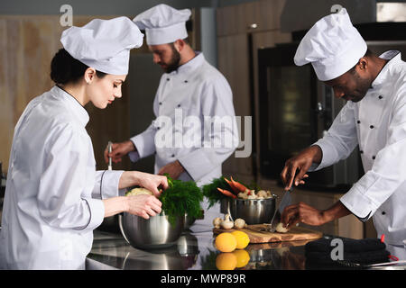 Gemischtrassiges Team von Köchen kochen durch die Küche im Restaurant Stockfoto