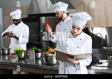 Köchin schreiben in Rezeptbuch von Ihrem multirassischen Kollegen Stockfoto