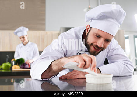 Männliche Chef garnieren Teller auf Restaurant Küche vor der weiblichen Cook Stockfoto
