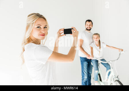 Glückliche junge Frau fotografieren Familie mit Smartphone isoliert auf weißem Stockfoto