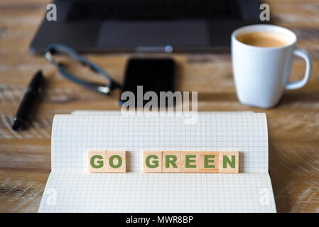 Nahaufnahme auf das Notebook um Holz Tisch Hintergrund, auf Holzblöcken mit Buchstaben, Go Green Text konzentrieren. Konzept Bild. Laptop, Brille, Stift- und Mobi Stockfoto