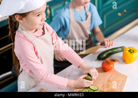 7/8 Schuß von niedlichen kleinen Kinder in Schürzen Kochen Gemüse Salat zusammen in der Küche Stockfoto