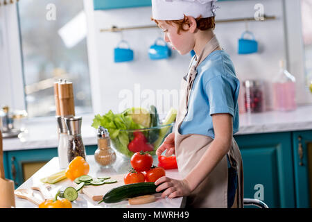 Seitenansicht des niedlichen kleinen Jungen in Chef hat und Schürze Kochen in der Küche Stockfoto