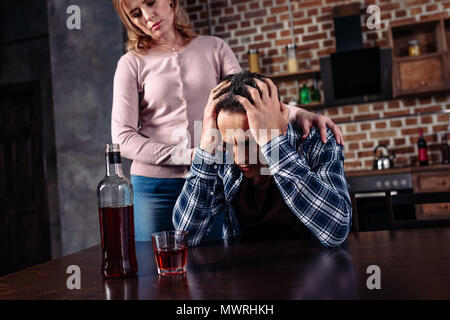 Betrunkener mann am Tisch sitzen, während Frau stand in der Nähe von zu Hause. Stockfoto