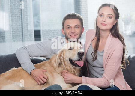 Junges Ehepaar sitzen auf der Couch im Wohnzimmer, einen Streichelzoo Hund und Kamera Stockfoto