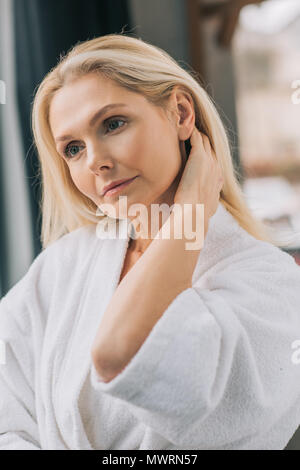 Wunderschöne reife Frau im Bademantel Hals berühren. Stockfoto