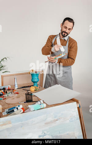 Lächelnd reife männliche Künstler in Schürze holding Palette in art studio Stockfoto