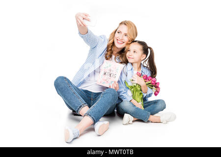 Lächelnde Mutter mit Postkarte und Tochter mit Blumen unter selfie zusammen isoliert auf weißem, Muttertag urlaub Konzept Stockfoto