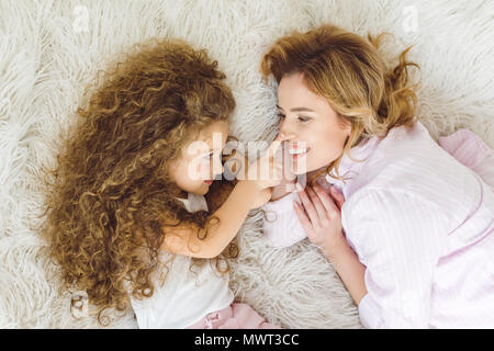 Blick von oben auf die bezaubernde curly Tochter ihrer Mutter Nase berühren. Stockfoto