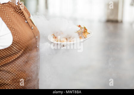 Junger Kellner mit Platte voller leckeren Törtchen bei Party Stockfoto