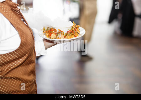 Junger Kellner mit Platte voller leckeren Törtchen bei Party Stockfoto