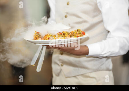 Junger Kellner mit Platte voller leckeren Törtchen bei Party Stockfoto