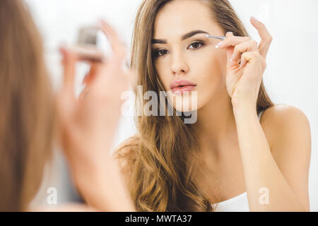 Junge Frau Zupfen der Augenbrauen mit Pinzette Stockfoto