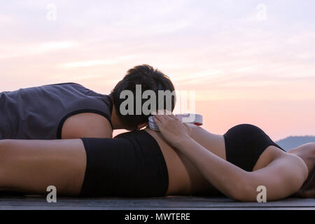 Schwangere Frau Kopfhörer auf dem Bauch und man Musik auf dem Boden am Berg Sonnenuntergang Zeit hören, Erwartung Konzept Stockfoto