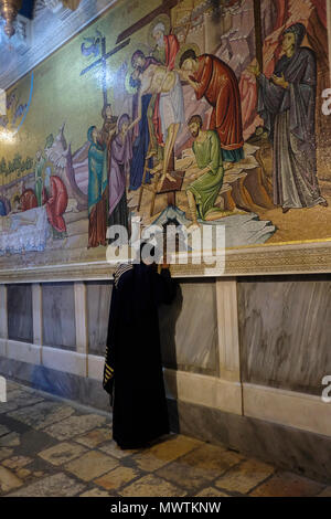 Ein christlich-äthiopisch-orthodoxer Pilger betet vor einem Wandmosaik, das den Körper Jesu Christi darstellt, der nach seinem Tod vorbereitet wird, gegenüber dem Stein von Anointing.inside die Grabeskirche in der Altstadt des Christlichen Viertels Ostjerusalem Israel Stockfoto