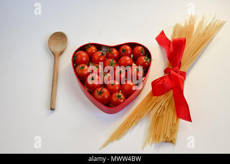 Holzlöffel, herzförmige Box von frischen Tomaten und ein Bündel von Ungekochten Spaghetti mit roter Schleife gebunden Stockfoto
