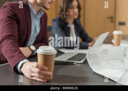 7/8 Schuß von Geschäftsleuten mit Papier Tassen Kaffee zusammen mit Laptop im Büro Stockfoto