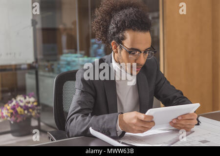 Konzentrierte sich der junge Architekt mit Tablet-PC am Arbeitsplatz in modernen Büro Stockfoto