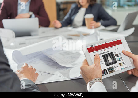 7/8 Schuß des Architekten mit Tablette mit der BBC-Website auf dem Bildschirm während Konferenz Stockfoto
