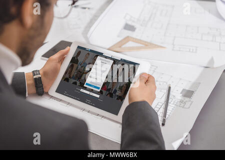 7/8 Schuß von jungen Architekten mit Tablet-PC am Arbeitsplatz Mit Linkedin website auf dem Bildschirm Stockfoto