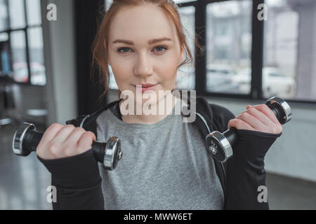 Übergewichtige Mädchen Hanteln und Kamera in der Turnhalle Stockfoto