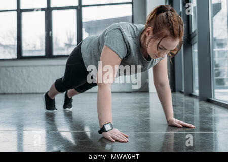 Übergewichtige Mädchen die Push-ups in der Turnhalle Stockfoto