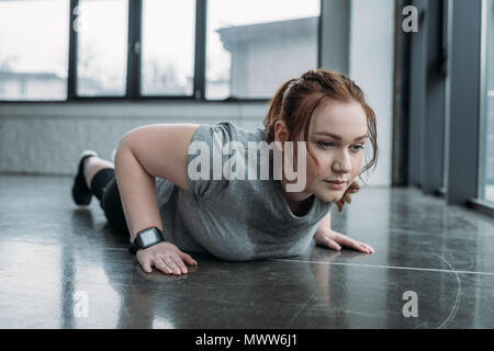 Übergewichtige Mädchen die Push-ups in der Turnhalle Stockfoto