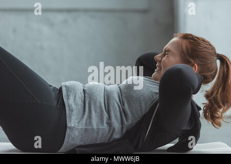 Übergewichtige Mädchen durchführen Sit Ups in der Turnhalle Stockfoto