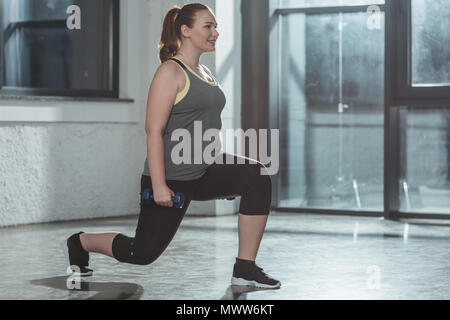 Übergewichtige Mädchen Ausfallschritte mit Hanteln in der Turnhalle Stockfoto