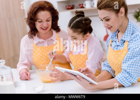 Großmutter und Enkelin zusammen kochen, während Mutter mit Tablette Küche Stockfoto