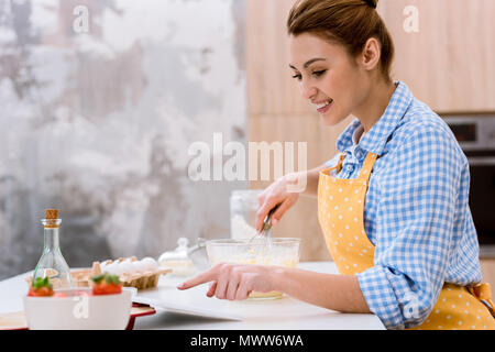 Attraktive junge Frau mit Tablette beim Kochen in der Küche Stockfoto