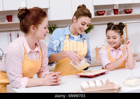 Drei Generationen von Frauen Teig in Backformen für Cupcakes in der Küche zusammen gießen Stockfoto