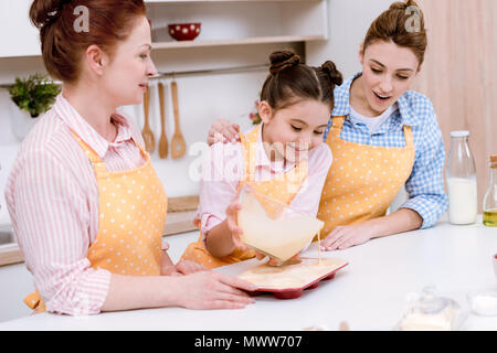 Drei Generationen von schönen Frauen Gießen Teig in Backformen für Cupcakes in Küche Stockfoto