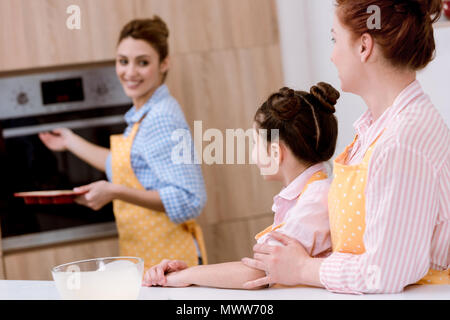 Drei Generationen von schönen Frauen in Schürzen Gebäck zusammen backen an Küche Stockfoto