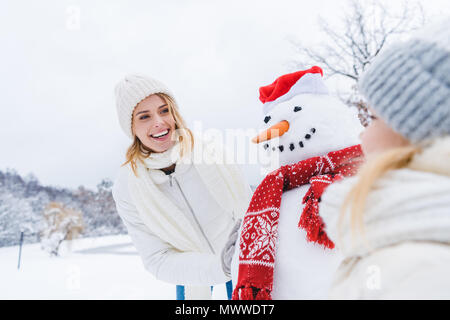 Glückliche Mutter und Tochter in der Nähe von Schneemann zusammen im Winter Wald Stockfoto