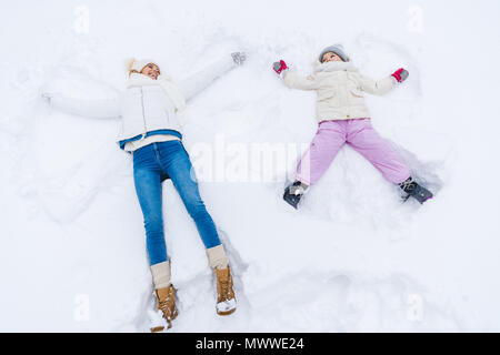 Hohe Betrachtungswinkel der glücklichen Mutter und Tochter machen Schnee Engel und lächeln einander Stockfoto