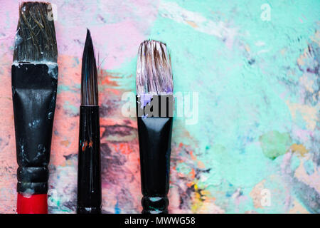 Nahaufnahme der künstlerischen Bürsten auf Palette mit bunten Farbflecken abgedeckt Stockfoto