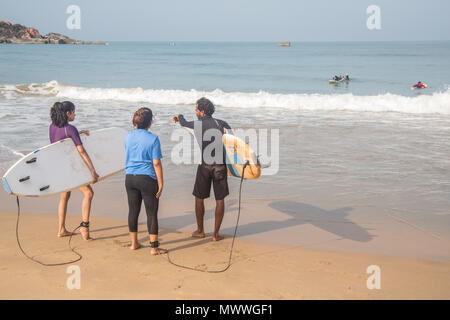 Surfen Studenten durch das Wasser an einem Strand in Goa, Indien, während eines frühen Sommer session. Stockfoto
