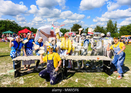 Welt Custard pie Meisterschaften, zwei Teams, "japanische Mädchen" und "Die Piebots', Team gekleidet, wie Silber Roberts, nachdem der Wettbewerb hinter Vanillepudding gedeckten Tisch und mit Platten von custard posieren. Draußen strahlender Sonnenschein, blauer Himmel mit weißen Wolken. Stockfoto