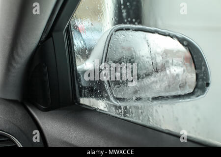 Blick aus dem Auto, auf der Suche nach Außenspiegel, nass vom Wasser und Seife in der Waschstraße gewaschen wird. Stockfoto
