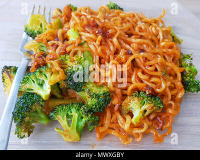 Ansicht von oben. Lecker. Spicy koreanischen instant Nudeln mit grünem Gemüse, auf Teller mit Gabel auf Holz Tisch mit Tageslicht Hintergrund Brokkoli. Stockfoto