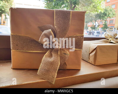 Große braune Gift box auf dem Tisch durch die klare Fenster befindet, Geschenkbox oder vorhanden mit Kraftpapier und einer großen Band umwickelt. Stockfoto